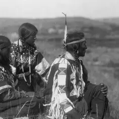Trzech Indian w tradycyjnych strojach, siedzących na trawie. Ciekawe detale zdobień ich ubrań.