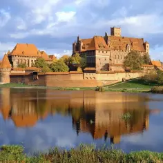 Potężny zamek w Malborku odbija się w spokojnej wodzie. Poznaj zamek w Malborku ciekawostki i jego historię.