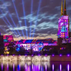 Nocne iluminacje na Ostrowie Tumskim we Wrocławiu. Kolorowe projekcje na budynkach i wieżach tworzą magiczny widok, a promienie światła sięgają nieba. Ciekawe ciekawostki o Wrocławiu można odkrywać podczas takich wydarzeń.