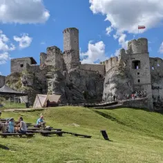Ruiny zamku na skale, część wyżyny krakowsko-częstochowskiej, z widownią siedzącą na trawie.