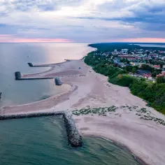 Jarosławiec molo chroni plażę przed falami. Widok z lotu ptaka na morze, plażę i zabudowania.