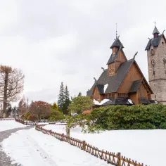 Karpacz, jakie to góry? To widok na drewniany kościółek Wang i kamienną wieżę, otoczone zimowym krajobrazem Karkonoszy.