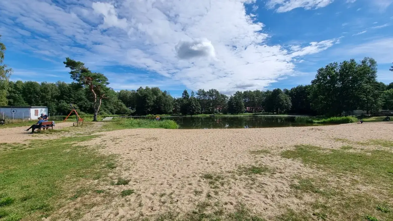 Plaża nad jeziorem, idealne miejsce na relaks. W tle las i błękitne niebo z chmurami. Bobolice atrakcje czekają!