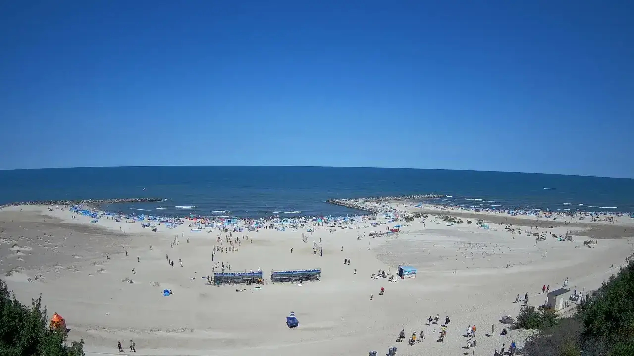 Słoneczny dzień na plaży w Jarosławcu. Tłumy plażowiczów, parasole i widoczny w oddali falochron.