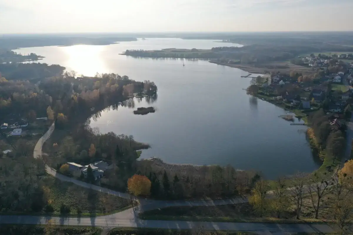 Jesioro Kałębie o poranku, z łódką na wodzie i jesiennymi kolorami drzew na brzegu.