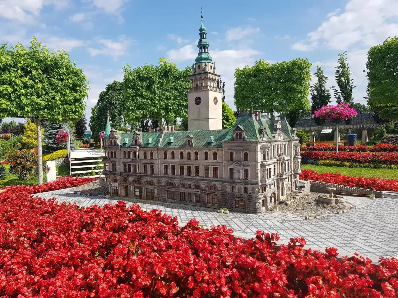 Miniatura ratusza w Kłodzku, otoczona czerwonymi kwiatami, stanowi serce kotliny kłodzkiej.
