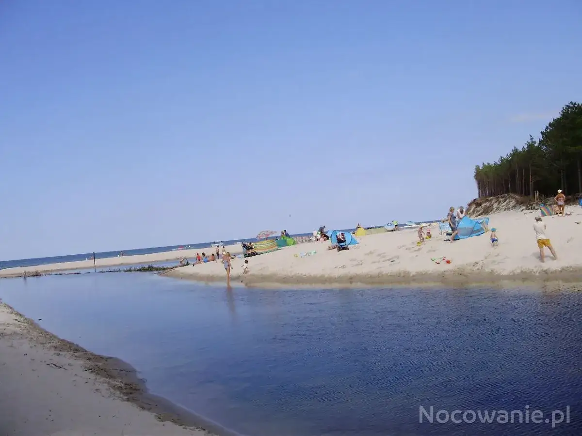 Słoneczna dębki plaża z turkusową wodą i ludźmi odpoczywającymi pod namiotami.