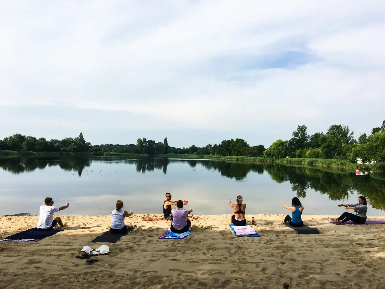 Jezierzany atrakcje: grupa osób ćwiczy jogę na piaszczystej plaży nad spokojnym jeziorem.