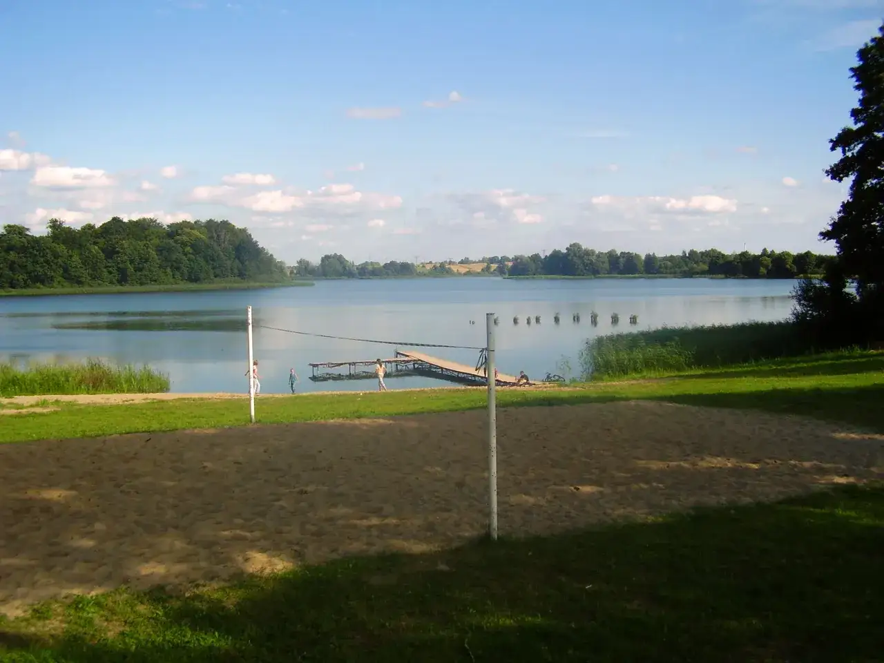 Piękny dzień nad jeziorem Skiertąg. Piaskowa plaża, pomost i zielone drzewa tworzą idylliczny krajobraz.