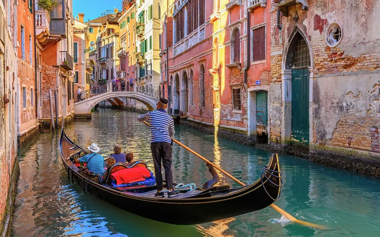 Gondola płynie kanałem w Wenecji, mieście zakochanych. W tle widać most i zabytkowe kamienice.