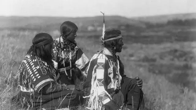 Trzech Indian w tradycyjnych strojach, siedzących na trawie. Ciekawe detale zdobień ich ubrań.